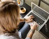 Femme tapant sur un ordinateur portable, une tasse de café à côté. Elle rédige peut-être une lettre recommandation locataire.