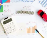 Calculatrice, pièces et voiture rouge sur des graphiques financiers. Idéal pour illustrer les frais de remboursement anticipé prêt immobilier.
