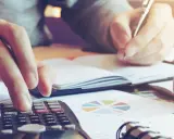 Calculatrice et stylo en main, une personne travaille sur un tableau d'amortissement d'un bien immobilier, entourée de graphiques.