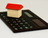 Maisonnette en bois sur calculatrice, symbolisant la régularisation de charges locatives tardives.