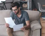 Homme concentré sur des documents, peut-être pour un crédit immobilier interimaire, assis sur un canapé.