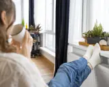 Une personne boit une tasse chaude, les pieds sur un radiateur, profitant de la chaleur. Un bon DPE chauffage électrique pour un confort optimal.