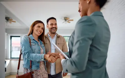 Un couple heureux serre la main d'une agente immobilière. Ils ont trouvé leur nouveau chez-soi, espérant que le loyer ne dépasse pas 3x leur salaire brut.
