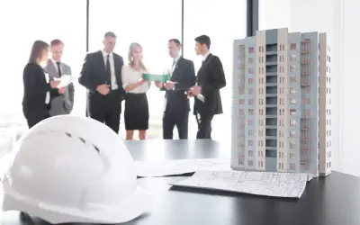 Maquette d'immeuble, plans et casque blanc sur une table. Des professionnels discutent, peut-être des travaux sur parties communes sans autorisation.