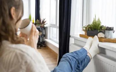 Une personne boit une tasse chaude, les pieds sur un radiateur, profitant de la chaleur. Un bon DPE chauffage électrique pour un confort optimal.