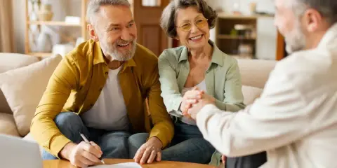 Couple âgé souriant discutant avec un conseiller, signature d'un prêt relais senior.