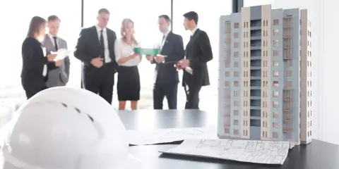 Maquette d'immeuble, plans et casque blanc sur une table. Des professionnels discutent, peut-être des travaux sur parties communes sans autorisation.