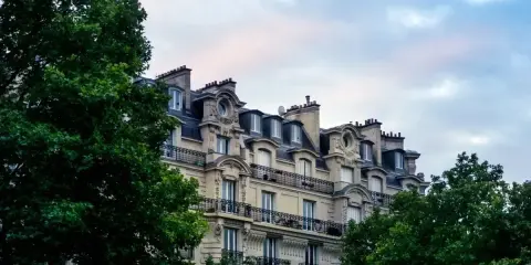 Immeuble haussmannien avec balcons en fer forgé, idéal pour une vente immeuble à rénover. Verdure luxuriante encadrant la façade.