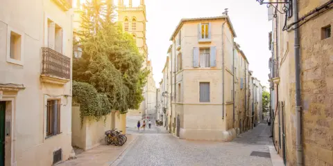 Ruelles pavées et bâtiments ocres, un aperçu des meilleurs quartiers de Montpellier. Des vélos attendent, des passants flânent sous le soleil.