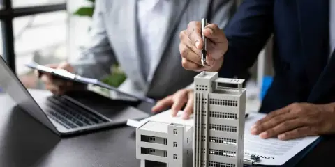 Deux personnes discutent de modèles de bâtiments et de documents, possiblement pour un projet immobilier ou un régime fiscal immobilier.