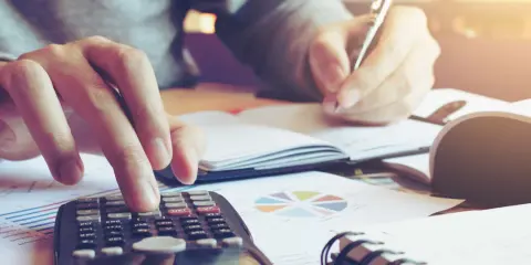 Calculatrice et stylo en main, une personne travaille sur un tableau d'amortissement d'un bien immobilier, entourée de graphiques.