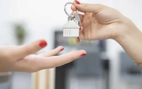 Une main tend des clés avec un pendentif maison. Le locataire reçoit les clés, prêt à emménager et à gérer ses impôts locaux.