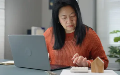 Femme calculant des frais de location avec un ordinateur portable et une calculatrice.