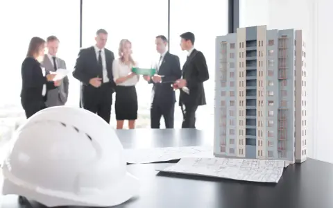 Maquette d'immeuble, plans et casque blanc sur une table. Des professionnels discutent, peut-être des travaux sur parties communes sans autorisation.
