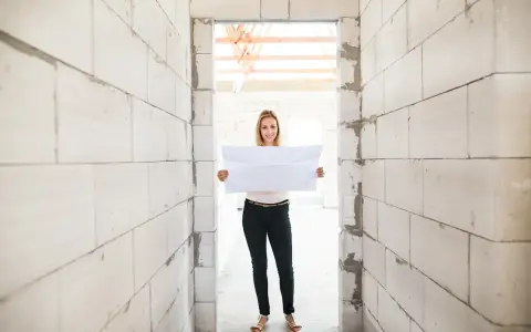 Femme souriante tenant un plan dans un chantier. Un acompte encaissé pour des travaux non réalisés, mais l'espoir est là.
