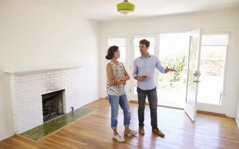 Un agent immobilier présente un appartement ou une maison à une cliente potentielle. La pièce est lumineuse, avec une cheminée en briques blanches et un sol en bois.
