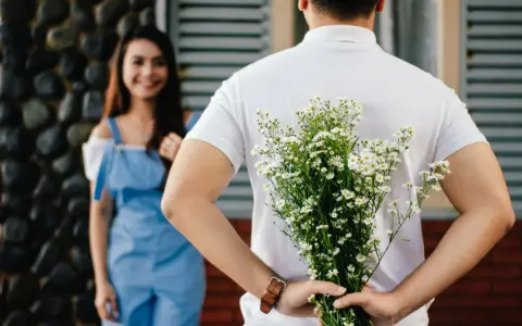 Un homme cache un bouquet de fleurs derrière son dos, prêt à surprendre sa compagne. Un couple non marié dans un lieu extérieur.