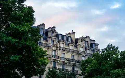 Immeuble haussmannien avec balcons en fer forgé, idéal pour une vente immeuble à rénover. Verdure luxuriante encadrant la façade.