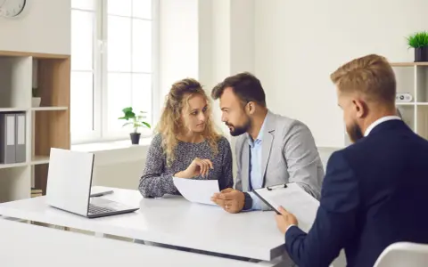 Un couple discute de documents avec un conseiller. Ils cherchent des solutions pour leur reste à vivre, une personne.
