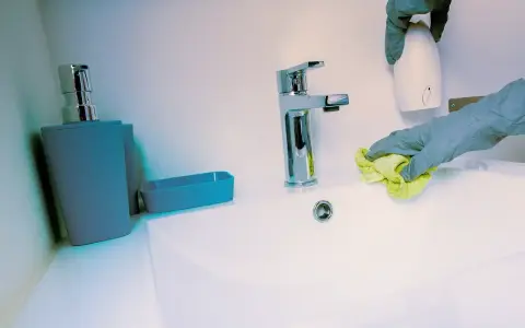 Mains de nettoyage avec un chiffon jaune, une retenue sur caution pour nettoyage. Un distributeur de savon et un robinet chromé sont visibles.