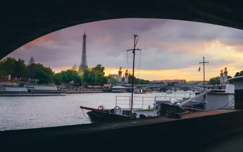 Vue de Paris au coucher du soleil, avec la Tour Eiffel en arrière-plan. Une péniche est amarrée, offrant un aperçu de la vie sur l'eau.