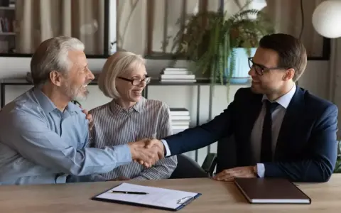 Un couple âgé serre la main d'un homme en costume. Ils sont co-emprunteurs mais pas propriétaires, un accord financier est signé.