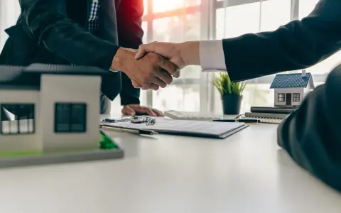Poignée de main entre deux hommes d'affaires, symbolisant la réussite de la vente de son appartement. Maquettes de maisons sur la table.
