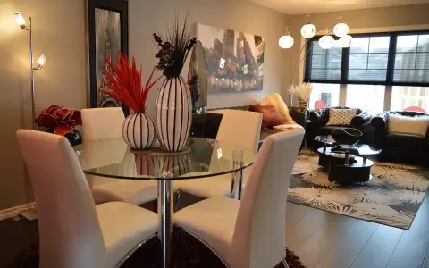 Table à manger moderne avec chaises blanches, parfaite pour une lmnp residence secondaire. Salon cosy avec canapés en cuir et tapis graphique.
