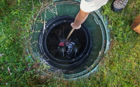 Vidange fosse septique avant le départ du locataire. Un homme utilise un outil pour nettoyer le fond de la fosse.