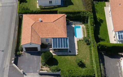 Vue aérienne d'une maison avec piscine et véranda. Une dépendance maison impôts, un garage et une allée complètent le paysage.