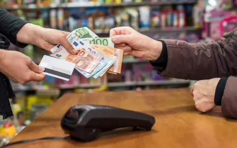 Une main tend des billets en euros et une carte bancaire. La question est : peut-on payer un artisan en liquide ?