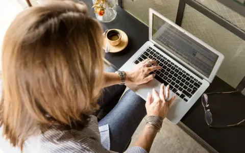 Femme tapant sur un ordinateur portable, une tasse de café à côté. Elle rédige peut-être une lettre recommandation locataire.