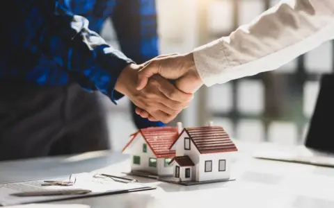 Poignée de main sur des maquettes de maisons, symbolisant un accord. Le compromis de vente délai dépassé par le vendeur est une préoccupation.