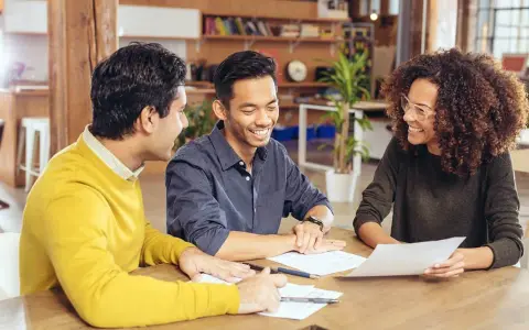 Trois personnes discutent autour d'une table, examinant des documents. Ils semblent planifier leur projet et se demandent combien emprunter avec 2500 euros par mois.