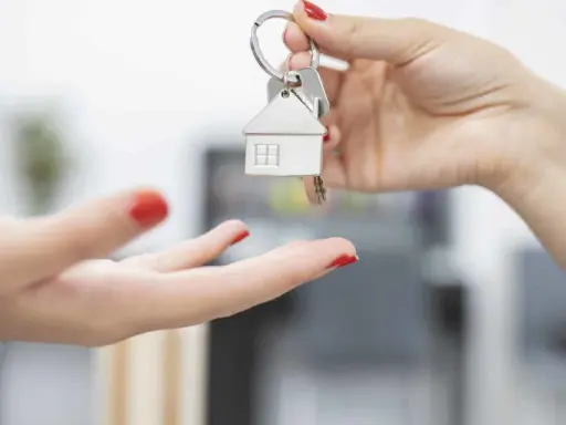 Une main tend des clés avec un pendentif maison. Le locataire reçoit les clés, prêt à emménager et à gérer ses impôts locaux.