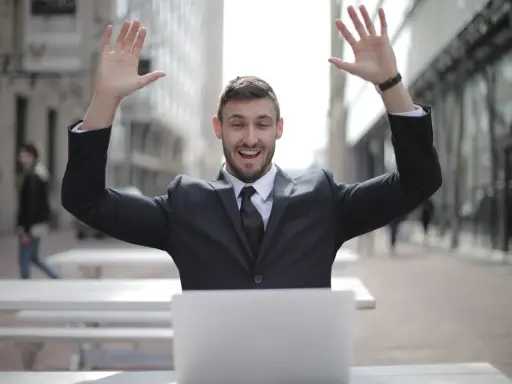 Homme en costume, bras levés, devant un ordinateur. Il semble avoir trouvé quel salaire pour emprunter 400 000 euros.
