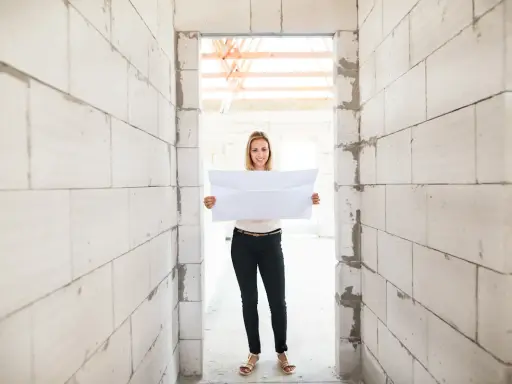 Femme souriante tenant un plan dans un chantier. Un acompte encaissé pour des travaux non réalisés, mais l'espoir est là.