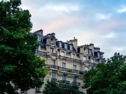 Immeuble haussmannien avec balcons en fer forgé, idéal pour une vente immeuble à rénover. Verdure luxuriante encadrant la façade.
