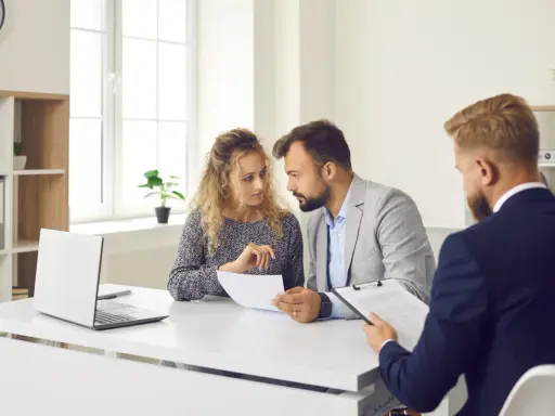 Un couple discute de documents avec un conseiller. Ils cherchent des solutions pour leur reste à vivre, une personne.