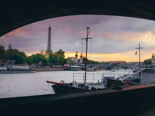 Vue de Paris au coucher du soleil, avec la Tour Eiffel en arrière-plan. Une péniche est amarrée, offrant un aperçu de la vie sur l'eau.