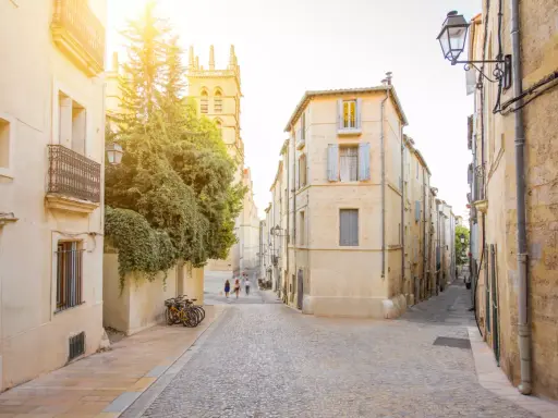 Ruelles pavées et bâtiments ocres, un aperçu des meilleurs quartiers de Montpellier. Des vélos attendent, des passants flânent sous le soleil.