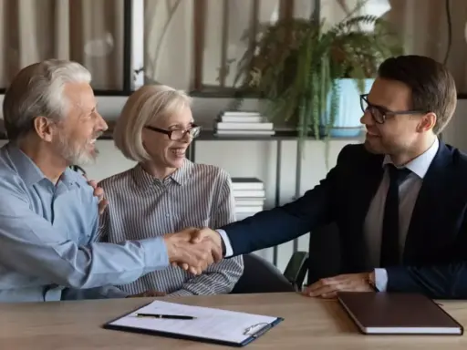 Un couple âgé serre la main d'un homme en costume. Ils sont co-emprunteurs mais pas propriétaires, un accord financier est signé.