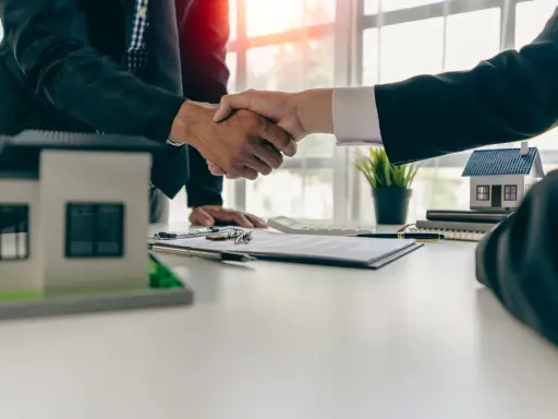 Poignée de main entre deux hommes d'affaires, symbolisant la réussite de la vente de son appartement. Maquettes de maisons sur la table.