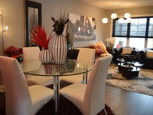 Table à manger moderne avec chaises blanches, parfaite pour une lmnp residence secondaire. Salon cosy avec canapés en cuir et tapis graphique.