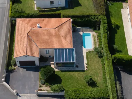 Vue aérienne d'une maison avec piscine et véranda. Une dépendance maison impôts, un garage et une allée complètent le paysage.