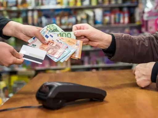 Une main tend des billets en euros et une carte bancaire. La question est : peut-on payer un artisan en liquide ?
