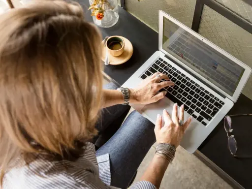 Femme tapant sur un ordinateur portable, une tasse de café à côté. Elle rédige peut-être une lettre recommandation locataire.