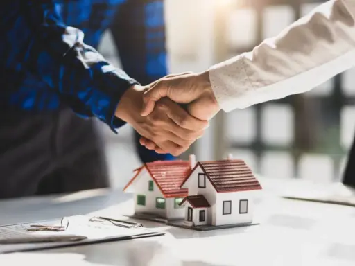 Poignée de main sur des maquettes de maisons, symbolisant un accord. Le compromis de vente délai dépassé par le vendeur est une préoccupation.