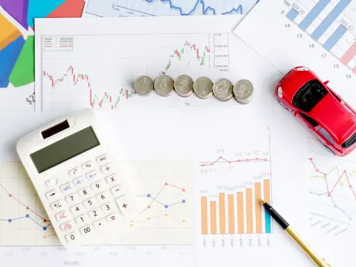 Calculatrice, pièces et voiture rouge sur des graphiques financiers. Idéal pour illustrer les frais de remboursement anticipé prêt immobilier.