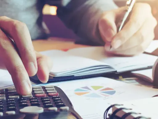 Calculatrice et stylo en main, une personne travaille sur un tableau d'amortissement d'un bien immobilier, entourée de graphiques.